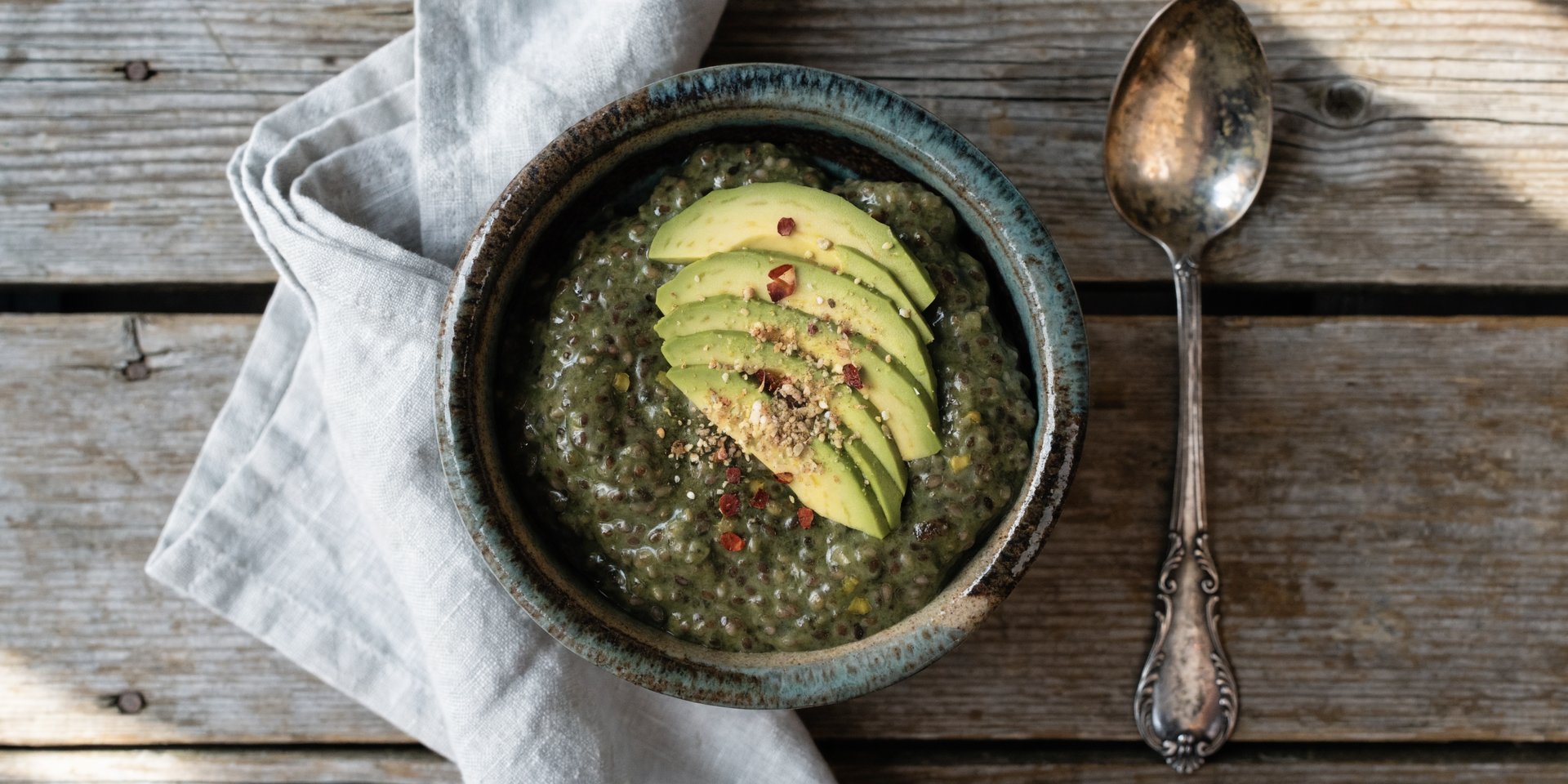 Green savory chia pudding in a rustic bowl with avocado, cherry tomatoes, and chili flakes